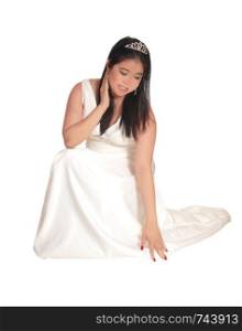 A gorgeous young bride in her white wedding dress crouching on the floor with a crown in her black hair, isolated for white background
