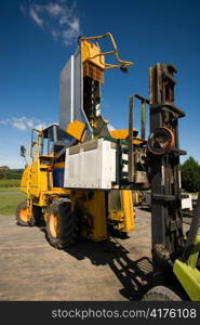 A grape harvester dumps its load of freshly picked grapes into a plastic bin supported by a forklift