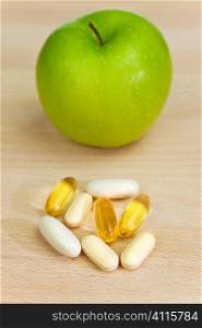 A green apple and tablets either medicinal pills or nutritional vitamin supplements. The focus is on the capsules pills and tablets in the foreground.
