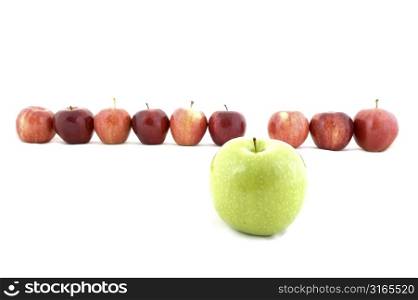A green apple stands out from the crowd of red apples