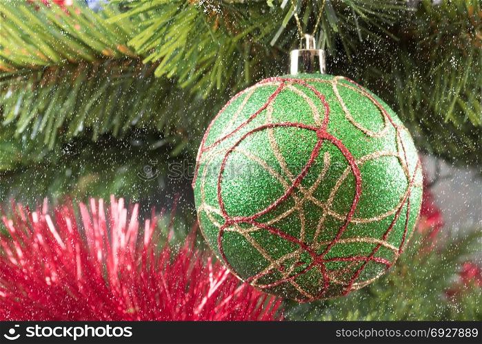 A green Christmas tree ball on a branch against the background of branches and a red garland