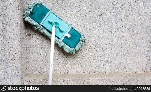 A green dirty mob or swab lean on dirty concrete wall. The floor mop is used to clean the floor clean. Cleaning and exercise by housework concept.