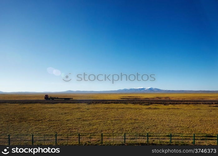 A green plains with a trailer and snow capped mountain in the background at Tibetan Plateau
