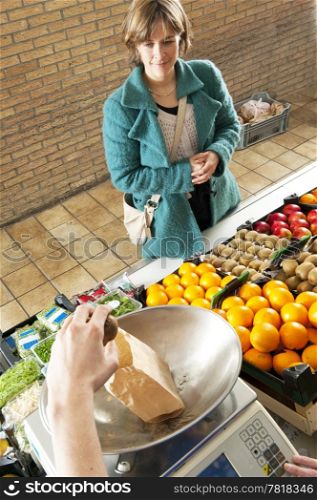 A greengrocer weighing a paper bag with kiwis for a customer