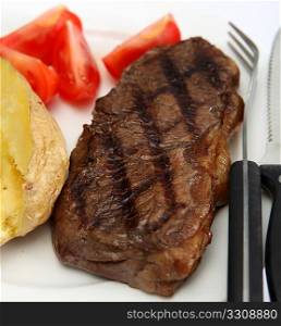 A grilled New York, striploin or porterhouse steak (names vary from place to place), served with baked potato and fresh tomato wedges.