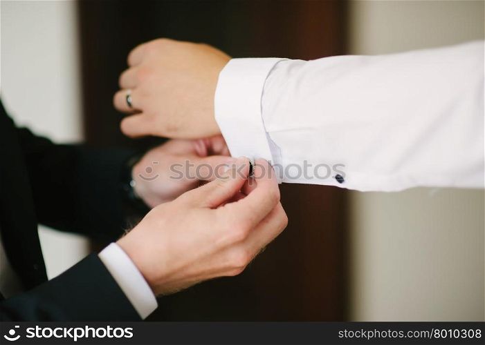 A groom fastening a cuff-link before getting married