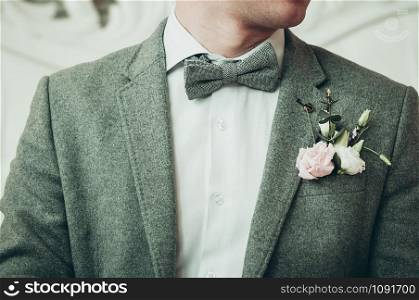 A groom in grey suit and white shirt preparing for the event, light background