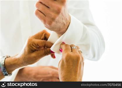 A groom putting on cuff-links as he gets dressed in his wedding day. A Groom&rsquo;s suit