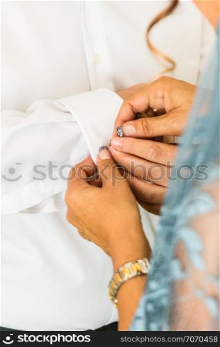 A groom putting on cuff-links as he gets dressed in his wedding day. A Groom&rsquo;s suit