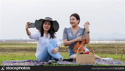 A group of Asian friends playing Ukelele and spending time making a picnic in the summer holidays.They are happy and selfie ,Relax time on holiday concept travel