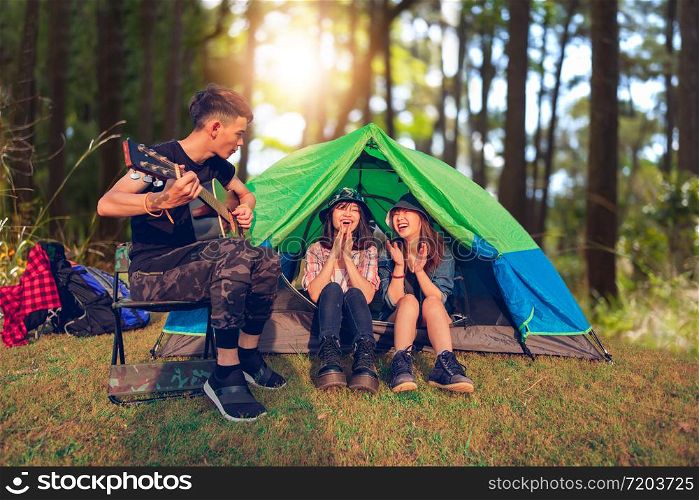 A group of Asian friends tourist drinking and playing guitar together with happiness in Summer while having camping