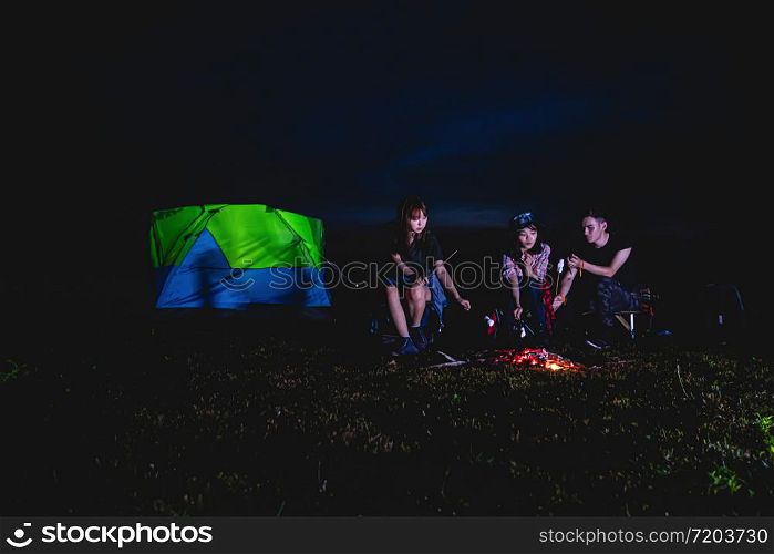 A group of Asian friends tourist drinking and playing guitar together with happiness in Summer while having camping near lake