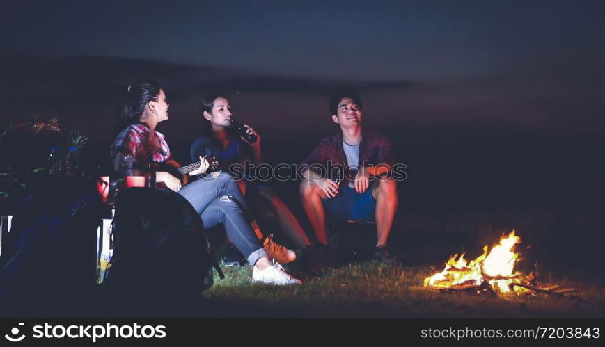 A group of Asian friends tourist drinking and playing guitar together with happiness in Summer while having camping near lake at sunset