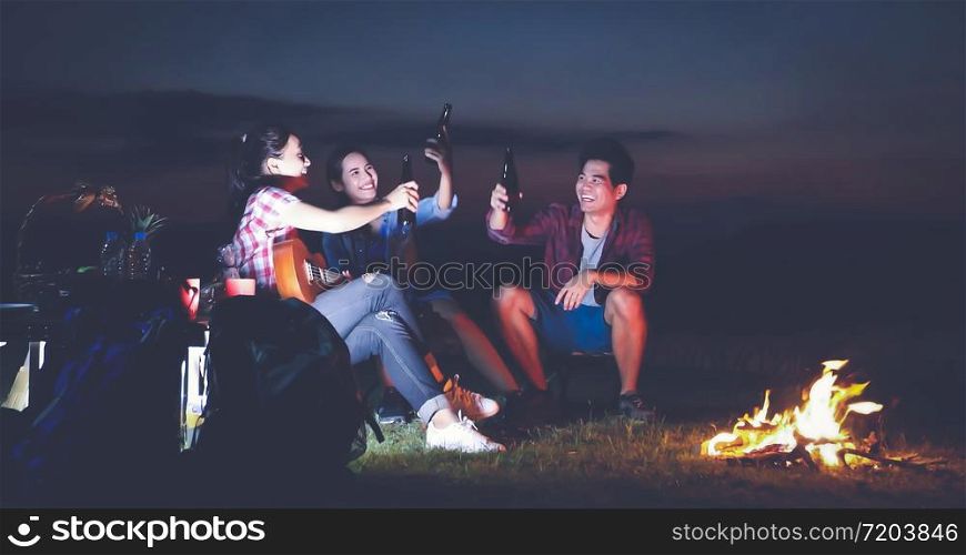 A group of Asian friends tourist drinking and playing guitar together with happiness in Summer while having camping near lake at sunset
