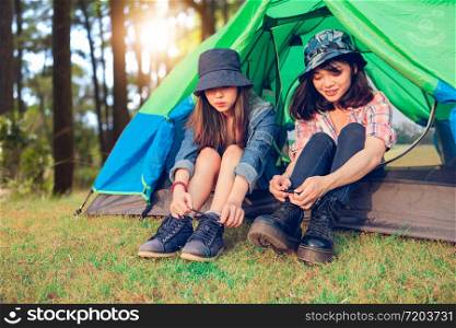 A group of Asian friends tourist Tie a shoe near tent with happiness in Summer while having camping