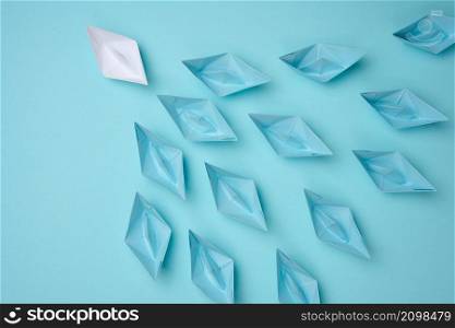 a group of blue paper boats follow white against a light blue background. Strong leader concept, mass manipulation. Starting a business with a well-coordinated team, start-up