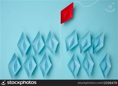 a group of blue paper boats heading in one direction and one red one heading in the opposite direction. The concept of individuality, uniqueness and talent of the employee. Get away from the influence