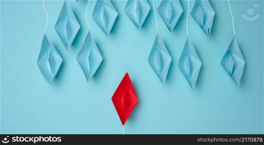 a group of blue paper boats heading in one direction and one red one heading in the opposite direction. The concept of individuality, uniqueness and talent of the employee. Get away from the influence