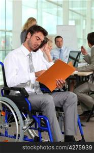 A group of business people in a meeting room, one of them in a wheelchair.