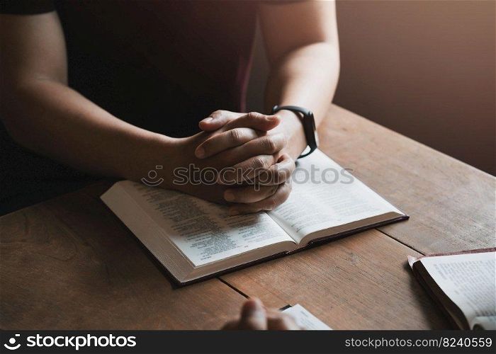 A group of Christians sit together and pray around a wooden table with blurred open Bible pages in their homeroom. Prayer for brothers, faith, hope, love, prayer meeting