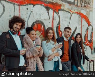 a group of diverse young businessmen on a break from work walk around the city, use smartphones, listen to music, and have fun. young people stand in front of a drawn wall in an abandoned street.