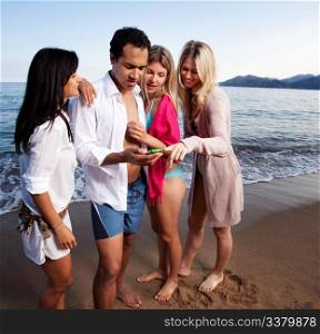 A group of friends looking at a cellphone at the beach