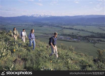A Group Of Hikers Walking Along A Grassy Ridge Overlooking A Mountain Valley