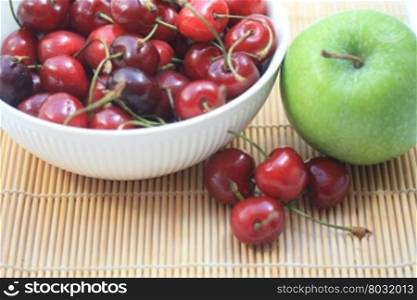 A group of juicy, fresh cherries in a white bowl and a green apple