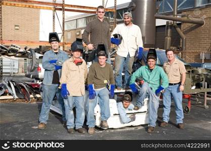 A group of metal workers posing with their supervisor in a scrap metal car.