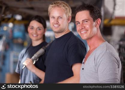 A group of three mechanics in a auto repair shop, looking at the camera