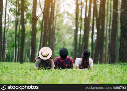 A group of travelers lying down on a green grass and looking into a beautiful pine woods