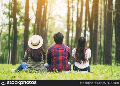 A group of travelers sitting on a green grass and looking into a beautiful pine woods