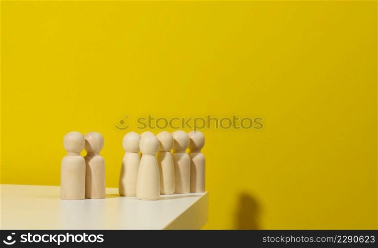 A group of wooden figurines on a yellow background. The concept of a strong leader, manipulation of the masses