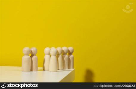 A group of wooden figurines on a yellow background. The concept of a strong leader, manipulation of the masses