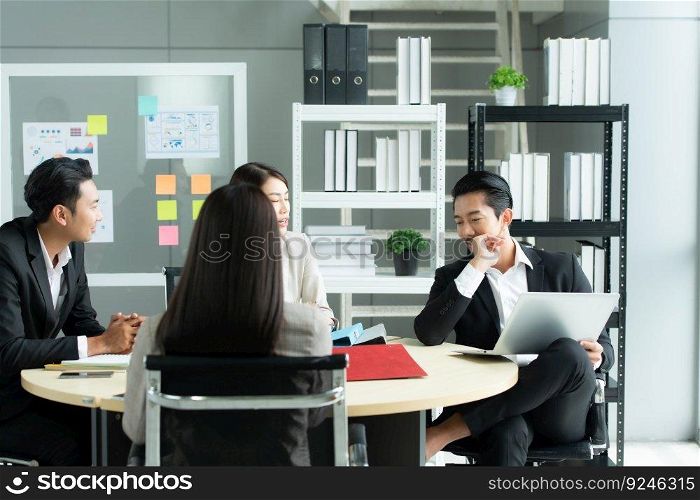A group of young Asian entrepreneurs. Top Management is meeting to review stock investment data from the team in a meeting room with natural light windows.