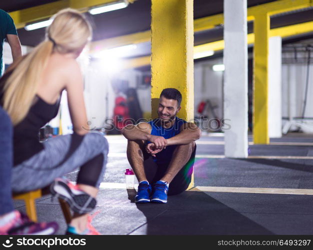 a group of young athletes sitting on the floor and relaxing after exercise at crossfitness gym. young athletes sitting on the floor and relaxing