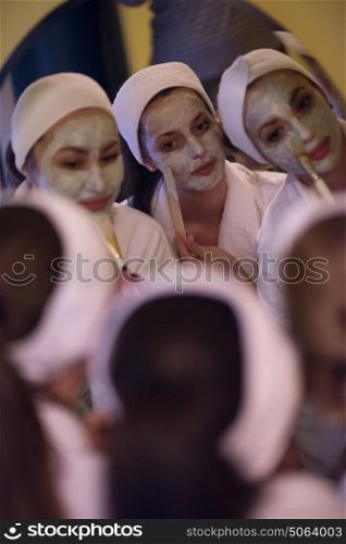 a group of young beautiful women looking in the mirror while putting face masks in the bathroom