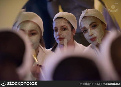 a group of young beautiful women looking in the mirror while putting face masks in the bathroom