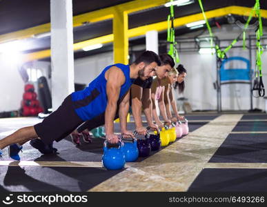 a group of young healthy athletes doing pushups with kettlebells at crossfitness gym. young athletes doing pushups with kettlebells