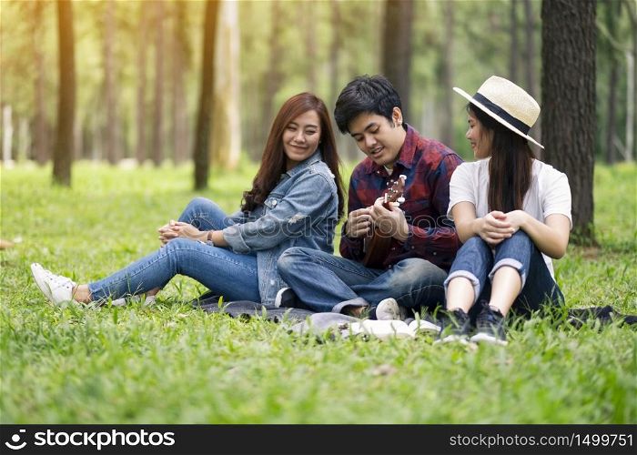 A group of young people playing ukulele while sitting together in the woods