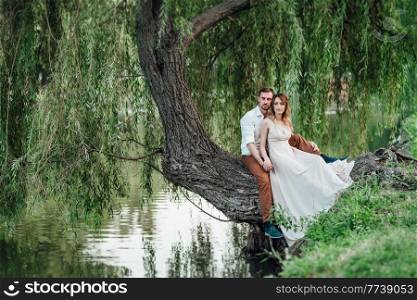 a guy and a girl are sitting together on a crooked tree on the steep bank of a wild river