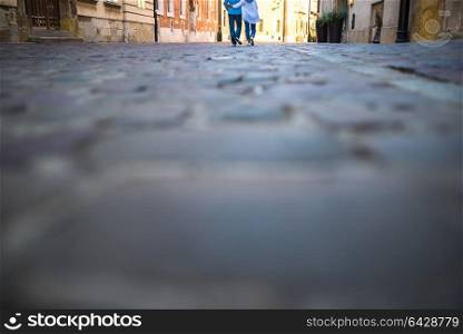 a guy and a girl are walking on an old cobblestone street in Europe