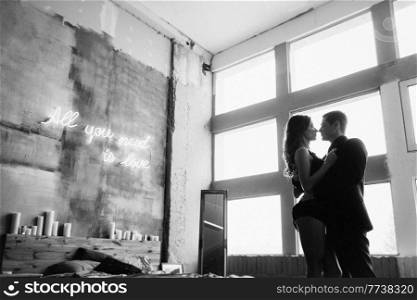a guy and a girl hug each other, standing in the bed and window