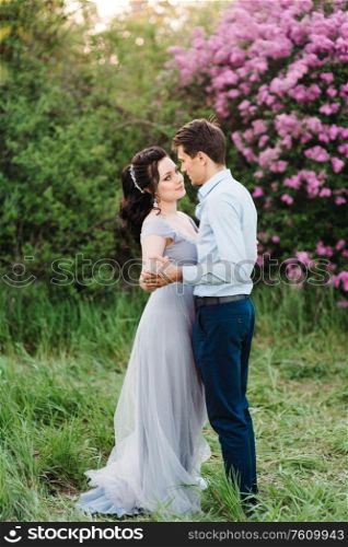 a guy and a girl walk in the spring garden of lilacs before the wedding ceremony