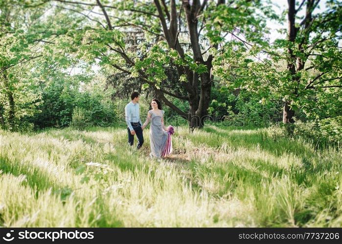 a guy and a girl walk in the spring garden of lilacs before the wedding ceremony