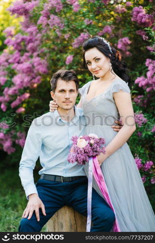 a guy and a girl walk in the spring garden of lilacs before the wedding ceremony