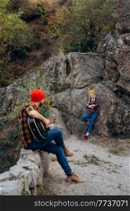 a guy in a bright hat plays the guitar with a girl against a background of granite rocks and a river