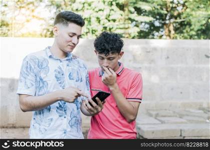 A guy showing his cell phone to another guy, Teenager explaining with his cell phone to another guy, A young man explaining with his cell phone to a young man