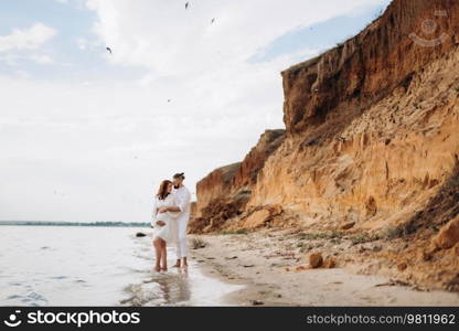 a guy with a girl in white clothes on the seashore next to clay cliffs