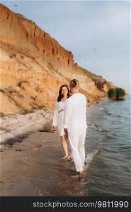 a guy with a girl in white clothes on the seashore next to clay cliffs